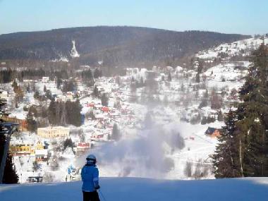 Skimausi vor Schneekanone mit Blick zum Aschberg