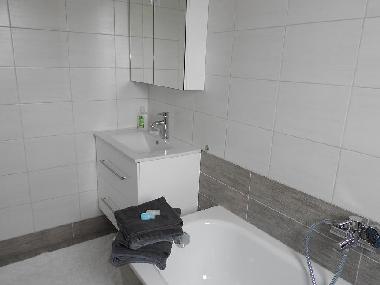 frisch renoviertes Badezimmer mit Badewanne und Waschbecken mit Schrank